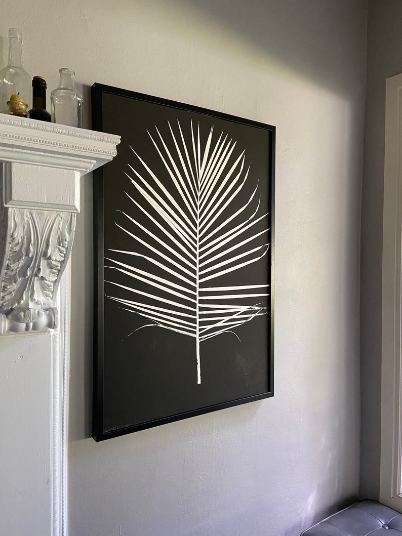 May include: Black and white framed print of a single palm leaf on a black background.