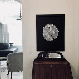 May include: A black framed print of a tree trunk cross section with visible rings. The print is hanging on a white wall above a dark wood desk with a mirror.