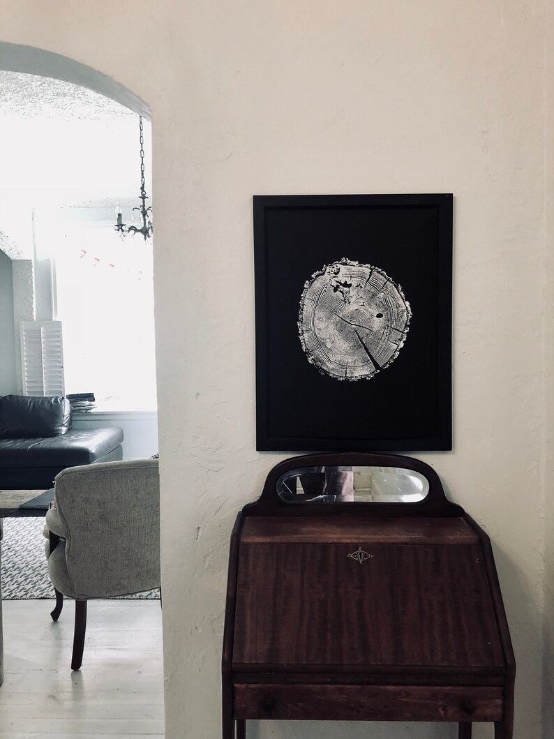 May include: A black framed print of a tree trunk cross section with visible rings. The print is hanging on a white wall above a dark wood desk with a mirror.