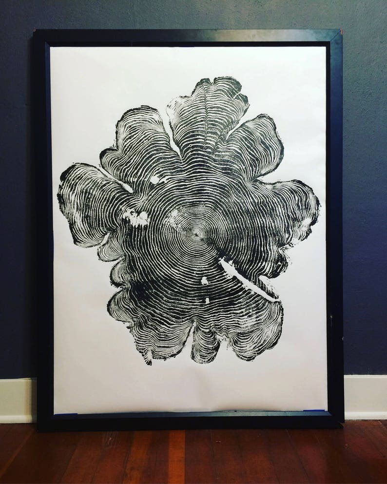 May include: Black and white print of a tree ring cross section. The print is framed in a black frame and is hanging on a wall.