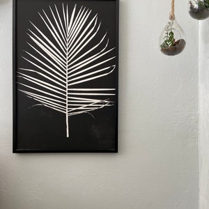 May include: Black and white framed print of a palm leaf silhouette on a black background.