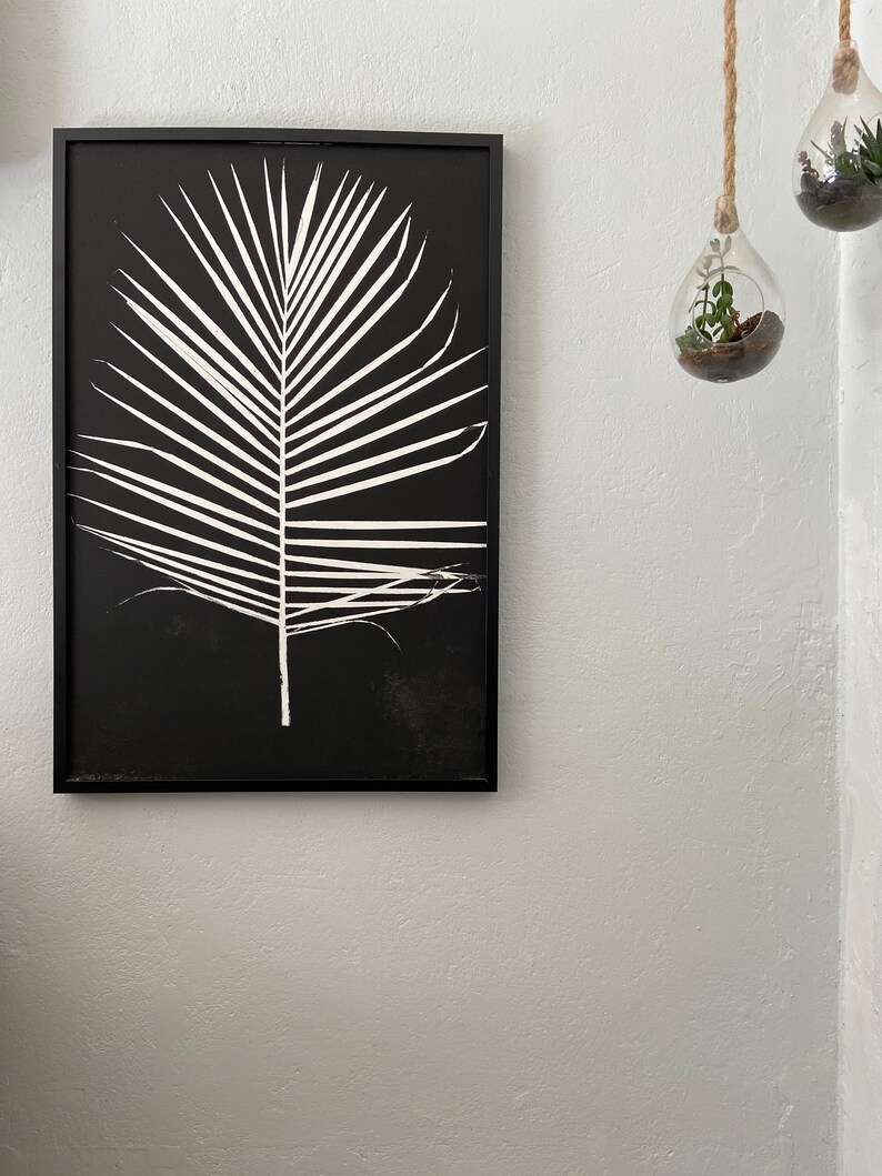 May include: Black and white framed print of a palm leaf silhouette on a black background.