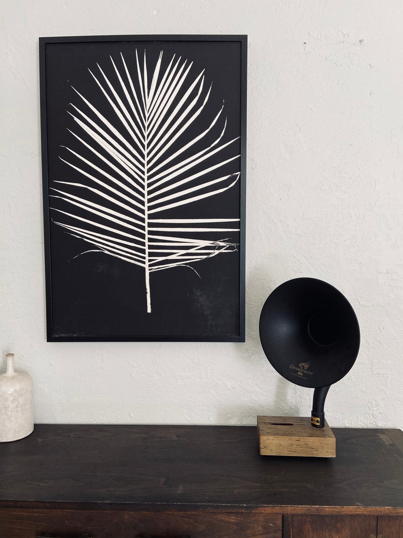 May include: A framed black and white print of a palm leaf with a vintage gramophone speaker on a dark wood surface.