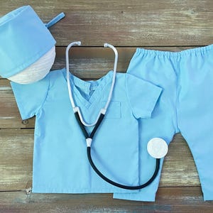 May include: A light blue doctor costume for kids, including a scrub top, pants, and a hat. The costume also includes a toy stethoscope.