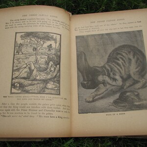 May include: An open book with black and white illustrations. The book is titled "The Three Clever Kings". The illustrations depict a man lying down under a tree and a cat with a boot.