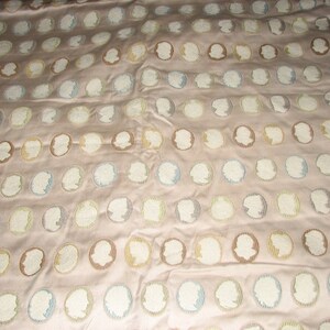 May include: A beige fabric with a repeating pattern of white, blue, and brown embroidered profile silhouettes.