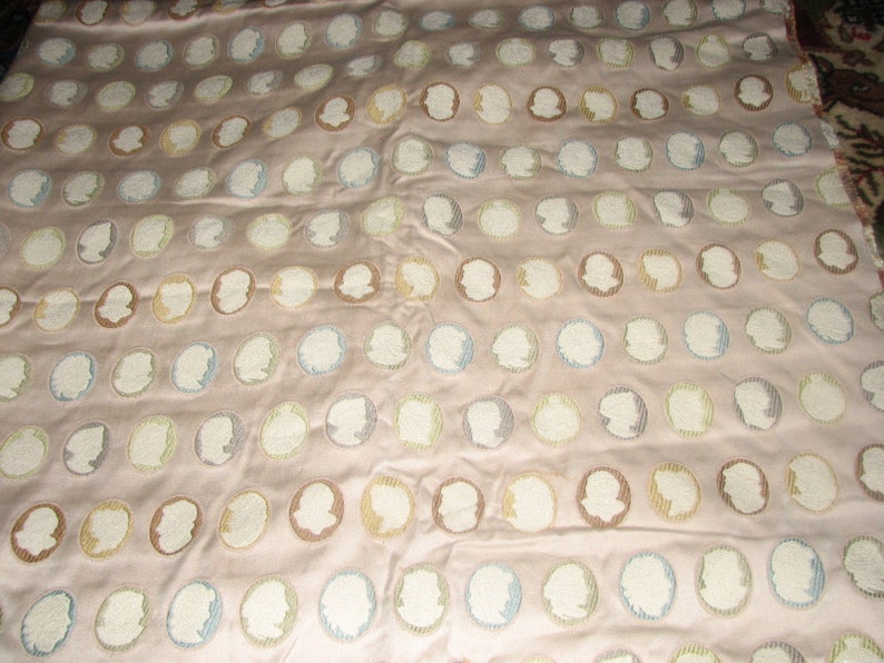 May include: A beige fabric with a repeating pattern of white, blue, and brown embroidered profile silhouettes.
