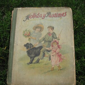 May include: A vintage children's book titled "Holiday Pastimes" with a green cover and illustrations of three children and a black dog. The children are wearing hats and are holding a bouquet of flowers, a stick, and a dog leash.