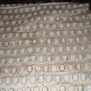 May include: A pink fabric with a repeating pattern of white oval shapes with a light blue, brown, or yellow silhouette of a person's face inside each oval.