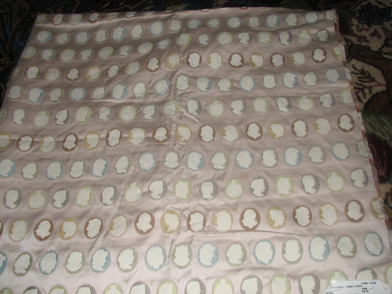 May include: A pink fabric with a repeating pattern of white oval shapes with a light blue, brown, or yellow silhouette of a person's face inside each oval.