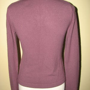 Puede incluir: Un su&eacute;ter malva con cuello y pu&ntilde;os de terciopelo. El cuello y los pu&ntilde;os est&aacute;n adornados con bordados dorados.