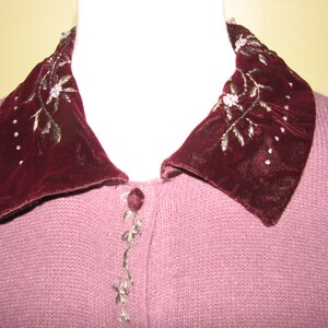 Puede incluir: Un c&aacute;rdigan de punto malva con un cuello grande de terciopelo burdeos con detalles florales bordados en hilo dorado.