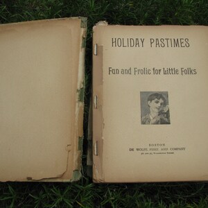 May include: A vintage book titled "Holiday Pastimes: Fun and Frolic for Little Folks" with a black and white illustration of a child on the cover. The book is published by De Wolfe, Fiske and Company in Boston.