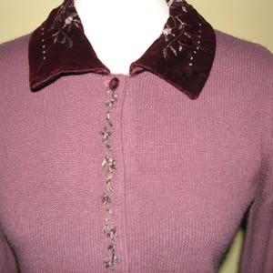 Puede incluir: Un c&aacute;rdigan de punto malva con un cuello de terciopelo que presenta detalles florales bordados en hilo dorado.
