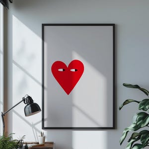 May include: A black framed print with a white background and a red heart with eyes. The heart is centred on the print.
