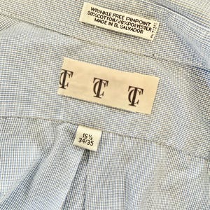 May include: Close-up of a light blue and white striped dress shirt. The shirt has a label that reads "WRINKLE FREE PINPOINT 80% COTTON/20% POLYESTER MADE IN EL SALVADOR." Another label displays the letters "TTT." A size label reads "16 1/2 34/35."