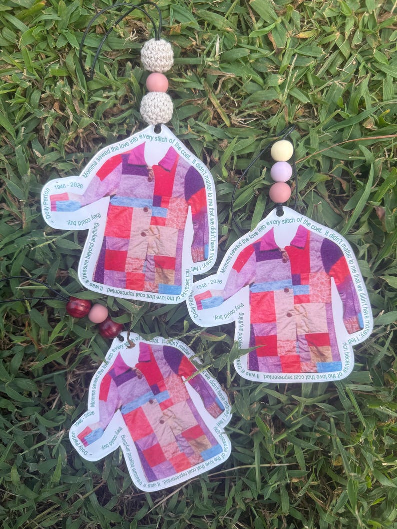 May include: Three hanging ornaments shaped like a patchwork coat with red, pink, and purple squares. Each ornament features the text "Momma sewed the love into every stitch of the coat. It didn't matter to me that we didn't have money. I felt rich because of the love that coat represented. It was a treasure beyond anything they could buy." and "Dolly Parton 1946-2026" with decorative beads.
