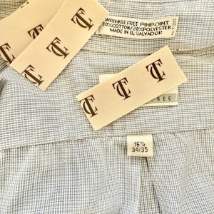 May include: Close-up of a light blue and white patterned dress shirt. The shirt has a classic collar and a label that reads "WRINKLE FREE PINPOINT 80% COTTON/20% POLYESTER MADE IN EL SALVADOR". The size tag reads 16 1/2 34/35.