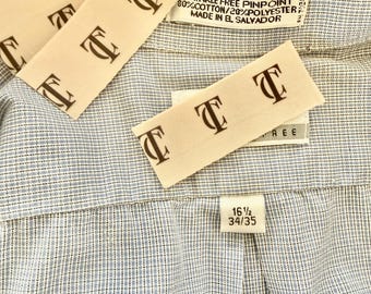 May include: Close-up of a light blue and white patterned dress shirt. The shirt has a classic collar and a label that reads "WRINKLE FREE PINPOINT 80% COTTON/20% POLYESTER MADE IN EL SALVADOR". The size tag reads 16 1/2 34/35.