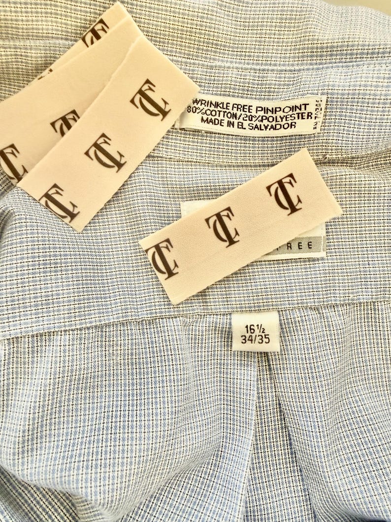 May include: Close-up of a light blue and white patterned dress shirt. The shirt has a classic collar and a label that reads "WRINKLE FREE PINPOINT 80% COTTON/20% POLYESTER MADE IN EL SALVADOR". The size tag reads 16 1/2 34/35.
