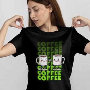 Könnte beinhalten: Schwarzes T-Shirt mit einer grün-weißen Grafik. Die Grafik zeigt das Wort "COFFEE" vertikal gestapelt, mit zwei lächelnden Kaffeetassen. Die Tassen haben Arme und sind mit Kaffee gefüllt.