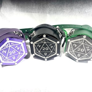 May include: Three leather dice bags in purple, black, and green. Each bag is shaped like a 20-sided die and has a silver engraved design.