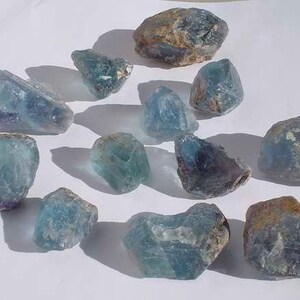 May include: A collection of 12 blue-green fluorite crystals of varying sizes and shapes. The crystals have a translucent appearance and show some natural inclusions.