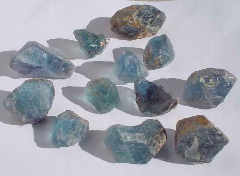 May include: A collection of 12 blue-green fluorite crystals of varying sizes and shapes. The crystals have a translucent appearance and show some natural inclusions.
