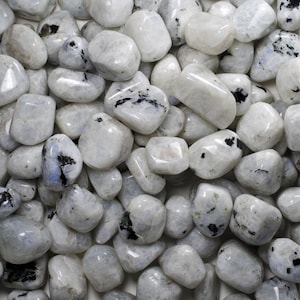 May include: A collection of white moonstone tumbled stones with black inclusions. The stones are smooth and polished, and they have a variety of shapes and sizes.