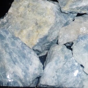 May include: A collection of rough, light blue celestite crystals. The crystals have a translucent, milky appearance and are arranged in a pile.
