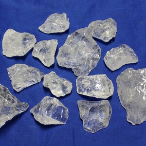 May include: A collection of clear quartz crystals of various sizes and shapes. The crystals are arranged on a blue background.