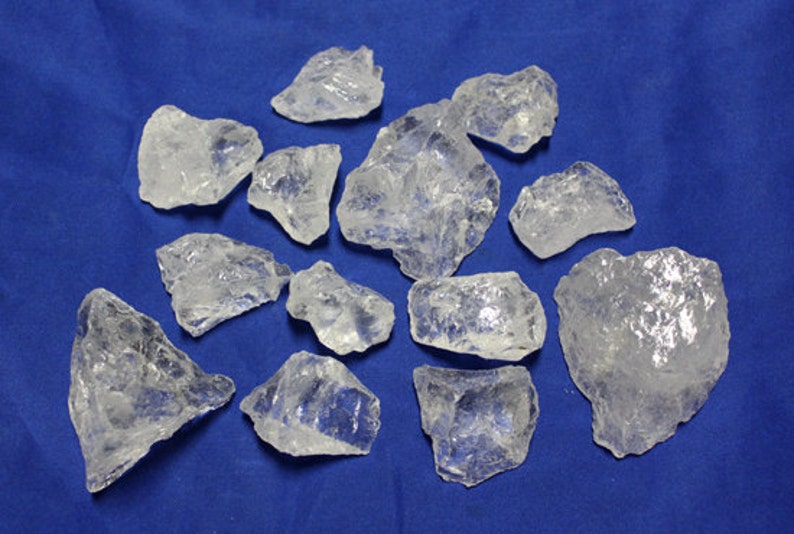 May include: A collection of clear quartz crystals of various sizes and shapes. The crystals are arranged on a blue background.