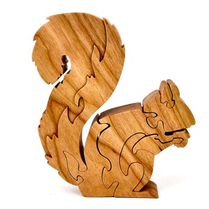 May include: A wooden squirrel puzzle with intricate details. The squirrel is made of light brown wood and has a bushy tail. The puzzle is made up of several pieces that fit together to form the squirrel.