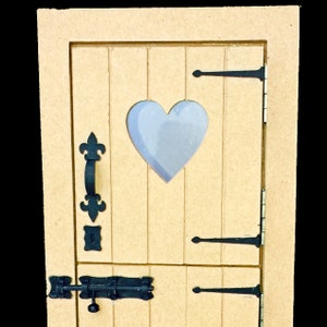 May include: A small wooden door with a light blue heart-shaped window. The door features black metal hinges, a handle, and a latch. It is constructed from light brown wood with vertical panels.
