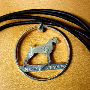 May include: A silver coin necklace featuring a Boxer dog silhouette cut out of the center. The coin is a US half dollar with the words "In God We Trust" visible on the edge.