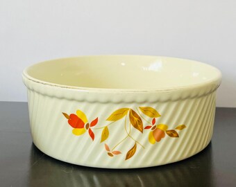 May include: Cream-colored, round ceramic baking dish with a floral design in orange, yellow, and brown. The dish has a ribbed exterior and a smooth interior. A vintage kitchenware item.
