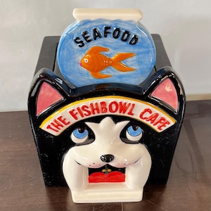 May include: A set of three ceramic mugs with a speckled, cream-colored glaze. Each mug features a different hand-painted design: a blue and green leaf, a yellow flower, and a red berry. The mugs have a simple, modern design.