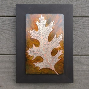 May include: A framed metal art piece featuring a detailed, silver-colored oak leaf on a copper background with shades of brown and orange.