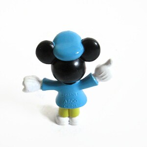 May include: A small Mickey Mouse figurine in a light blue outfit with a matching hat. The figure has black ears and a black face, with white gloves and yellow pants. The figurine is marked "Disney" and "ARGO CHINA".