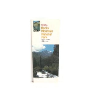 May include: A folded brochure with a landscape image and text. The brochure's cover features a small image of a lake and the text "Picture Taking in Rocky Mountain National Park". The brochure is white with a landscape image.