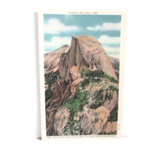 May include: Vintage postcard featuring a scenic view of Yosemite National Park. The image showcases a towering mountain with a prominent, rounded peak, lush green vegetation, and a blue sky with fluffy clouds. Text at the top reads "YOSEMITE NATIONAL PARK".