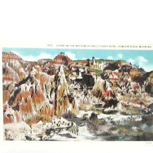 May include: Vintage postcard featuring a colorful landscape of Hell's Half Acre in Wyoming. The image showcases layered rock formations in shades of red, orange, and white under a blue sky. Text at the top reads "SCENE IN THE BOTTOM OF HELL'S HALF ACRE - POWDER RIVER, WYOMING."