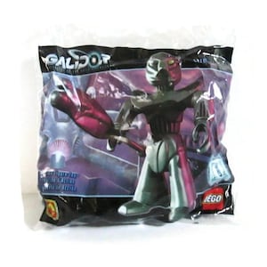 May include: A sealed plastic bag containing a Galidor action figure with a dark metallic finish and a large red accessory. The packaging features the Galidor logo at the top, a purple and black background design, and a small red LEGO logo in the corner.