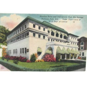 May include: Vintage postcard featuring the Maurice Baths and Therapeutic Pool in Hot Springs National Park, Arkansas. The building is a large, white structure with a green roof and awnings, surrounded by green grass and colorful flowers. Text on the postcard reads "U.S. Dept. of Interior."