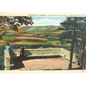 May include: A vintage postcard featuring a color illustration of the Overlook at Gambrill State Park, High Knob, near Frederick, MD. The scene shows two figures standing on a stone terrace overlooking a vast, rolling landscape of green fields.
