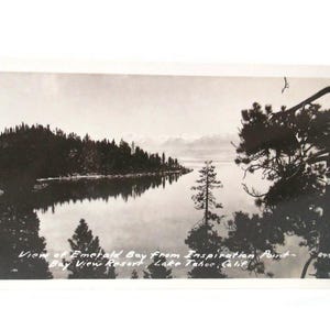 May include: Black and white vintage postcard featuring a scenic view of Emerald Bay from Inspiration Point, Lake Tahoe, California. The image shows a calm lake surrounded by trees and mountains, with text at the bottom.