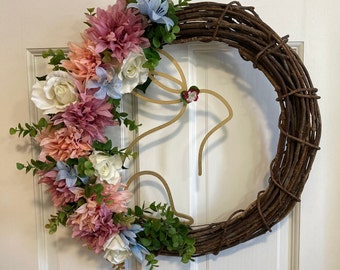 May include: A brown twig wreath decorated with pink, white, and blue artificial flowers. A gold metal bunny silhouette is attached to the wreath.