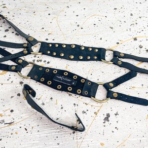 May include: Black leather harness with gold metal rings and studs. The harness has adjustable straps and buckles.