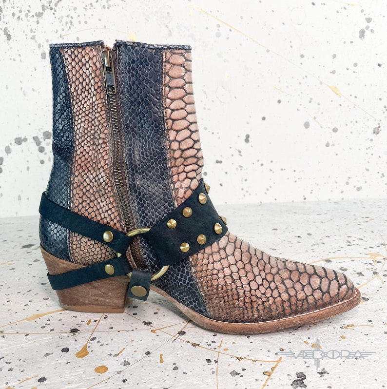 May include: Brown and black leather ankle boots with a snakeskin pattern and gold accents. The boots have a zipper on the side and a buckle strap with studs.