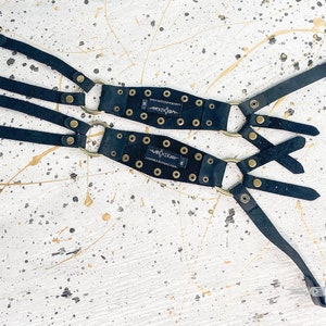 May include: Two black leather straps with gold metal rings and buckles. Each strap has a black leather patch with the word "Volition" printed in white.